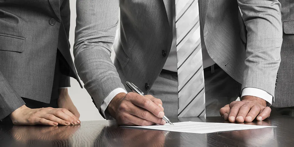 three people in suits with one signing a document